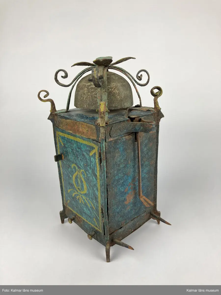 KLM 2798. Bordsur. Rektangulär stomme av järn med öppningsbara sidor. Upptill smidda detaljer samt ringklocka. På ena sidan urtavla av mässing med en visare av järn. Urverk av järn och mässing med släphaksgång. Fodralet är målat blått med gula kantlister, på sidoväggarna en lyra i gult. Uret har fyra fötter. På baksidan ögla av järn. En pendel av metall tillhör. Lodlinor, lod och trissor saknas.