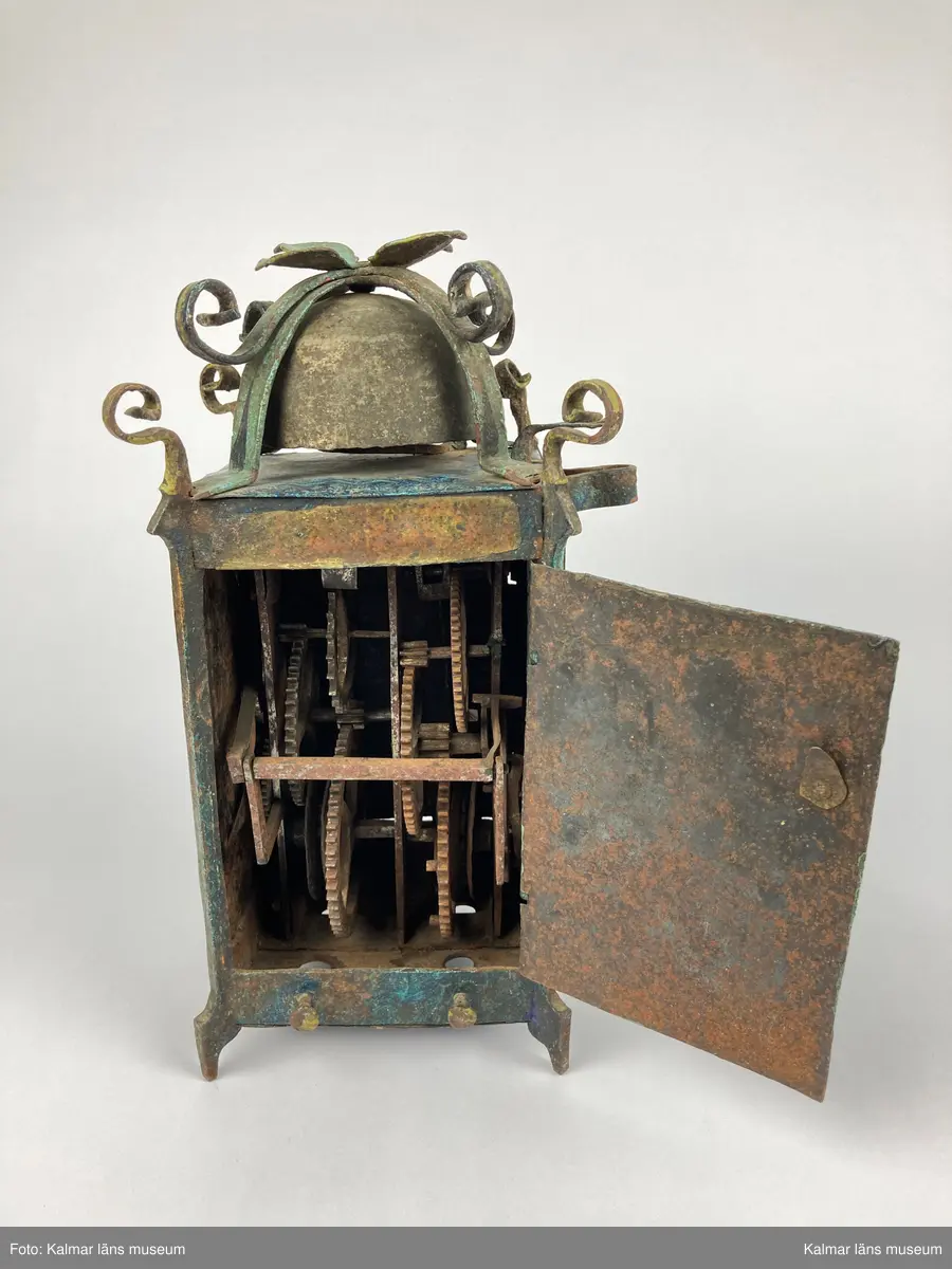 KLM 2798. Bordsur. Rektangulär stomme av järn med öppningsbara sidor. Upptill smidda detaljer samt ringklocka. På ena sidan urtavla av mässing med en visare av järn. Urverk av järn och mässing med släphaksgång. Fodralet är målat blått med gula kantlister, på sidoväggarna en lyra i gult. Uret har fyra fötter. På baksidan ögla av järn. En pendel av metall tillhör. Lodlinor, lod och trissor saknas.