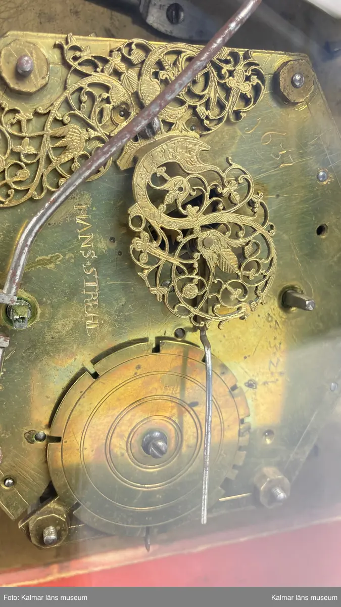 KLM 2269. Bordsur. Fodral av trä, lackerat i grönt med målade kinesiska figurer och landskap i svart och guld. Upptill handtag av mässing. Samtliga sidor är försedda med glaspartier och upptill mindre rutor med spegelglas. Både baksida och framsida kan öppnas. Vitmålad urtavla omgiven av bronsornament. Urverket av mässing och stål med rik ornering. Urverket är signerat: Hans Strehl 1637. Fodralet saknar fötter samt knoppar som suttit på ovansidan.