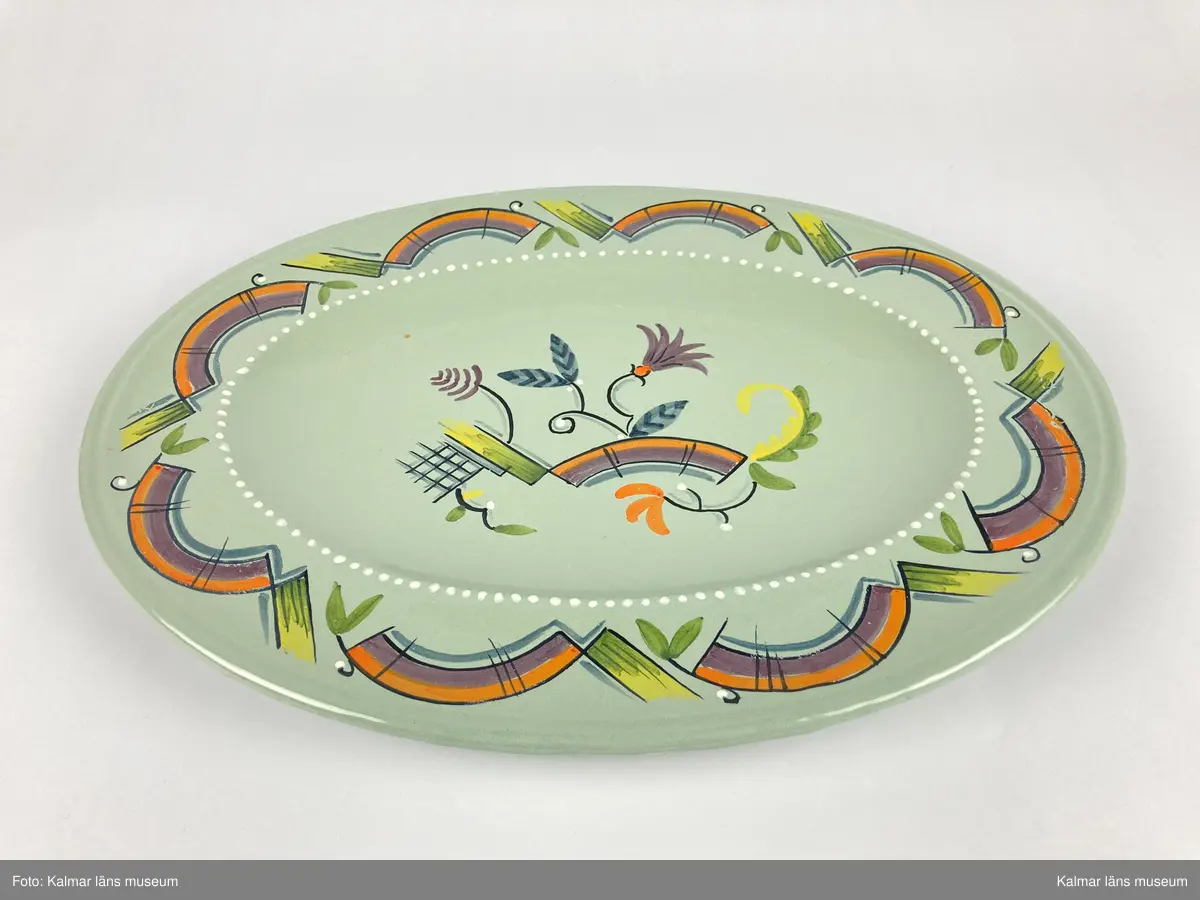 KLM 46967. Fat. Av fajans. Oval form med brätte. Glasyr i grått med målad dekor i bl.a. lila, orange, grönt och gult. Signerad på undersidan: Kalmar 1927 J.S. samt stämplad: SKAB 1878.