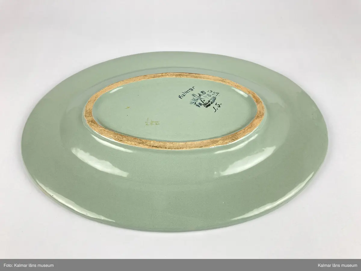 KLM 46967. Fat. Av fajans. Oval form med brätte. Glasyr i grått med målad dekor i bl.a. lila, orange, grönt och gult. Signerad på undersidan: Kalmar 1927 J.S. samt stämplad: SKAB 1878.