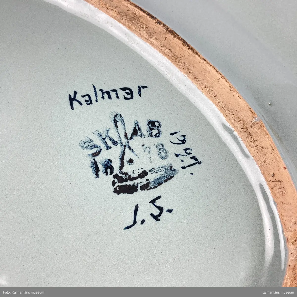 KLM 46967. Fat. Av fajans. Oval form med brätte. Glasyr i grått med målad dekor i bl.a. lila, orange, grönt och gult. Signerad på undersidan: Kalmar 1927 J.S. samt stämplad: SKAB 1878.