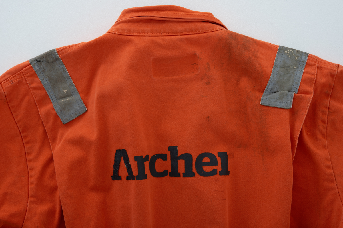 Kjeledress i størrelse 60 med Archer sin logo. Kjeledressen er utstyrt med flere utvendige lommer og reflekser. Innvendig i nakke er det festet en etikett med plattformnavn og QR-kode.