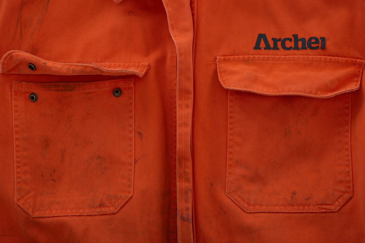 Kjeledress i størrelse 60 med Archer sin logo. Kjeledressen er utstyrt med flere utvendige lommer og reflekser. Innvendig i nakke er det festet en etikett med plattformnavn og QR-kode.