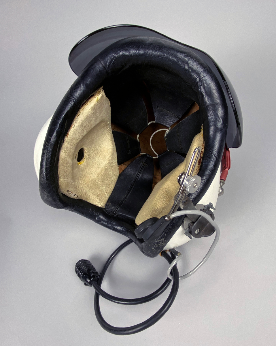 Flyghjälm 111, vit med tonat visir. Separat mikrofon monterad på vänster sida. Brytkoppelanslutning för kommunikation. Utskjutande form vid öronen, insida med förstärkt inlägg av skinn med skumgummifyllning. Hjälmen är försedd med röd metallräls runt hjässan. Skodd nederkant i svart skinn.