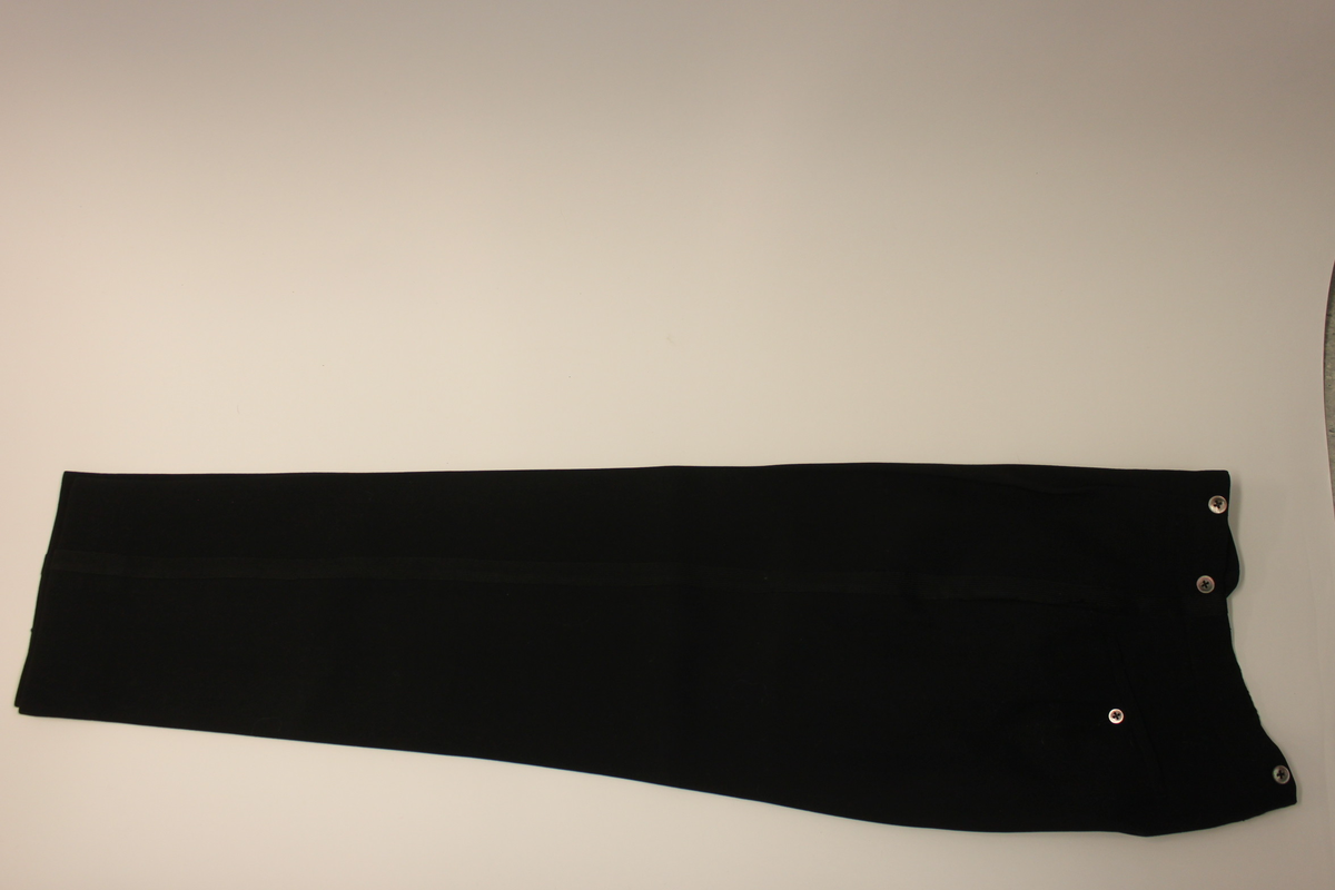 Svarta frackbyxor i ylle med revärer i svart silke. Knappar upptill för fästande av hängslen. Knapp på ficka samt gylf med dold knäppning.