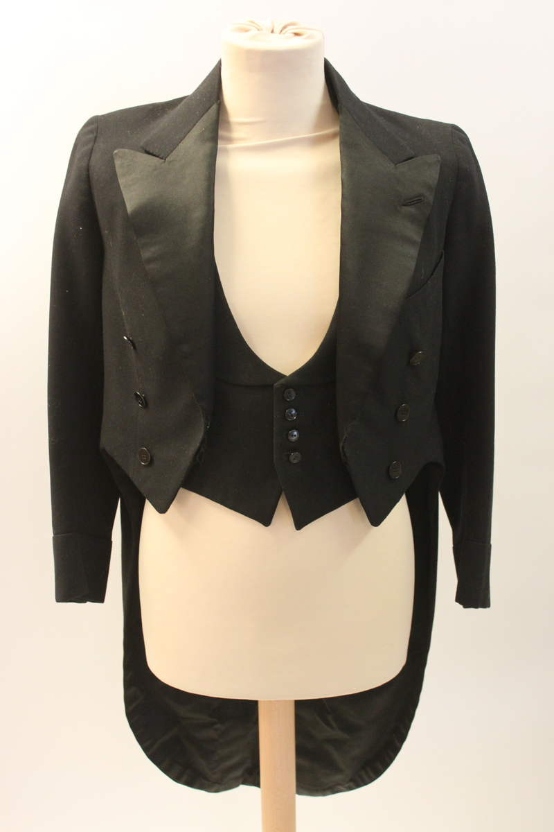 Frackrock, dubbelknäppt med sidenslag. Avskuren i midjan med delat skört bak.