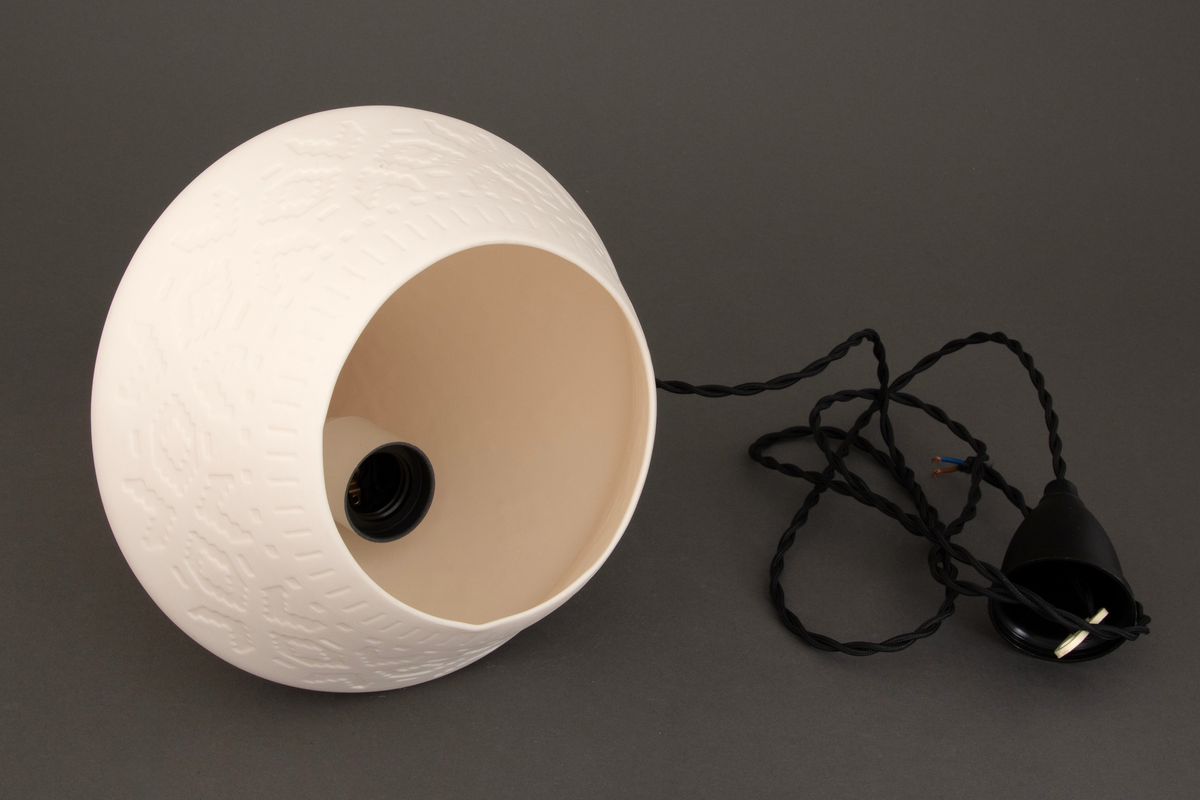 Lampens sandblåste mønster består av "strikkemasker", altså pikselerte punkter (kvadrater, "lus") som skal illudere mønstre fra strikkede klesplagg. En omsirklende rekke av åttebladsroser er det ornamentet som preger mønsteret mest, mens border og punkter er med og skaper assosiasjonene til plagg som gensere og votter. De tekstile referansene gir lampen en lun karakter, noe som forsterkes når lyset i den tennes.