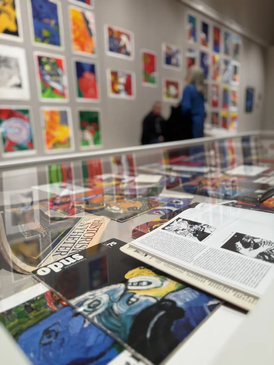 Monter med böcker i förgrund, i bakgrund vägg med litgografier