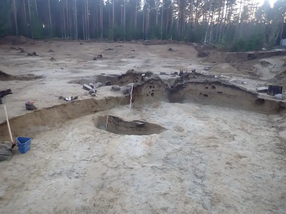 arkeologisk utgravning. Lys sand med mørke flekker etter forhistorisk aktivitet. 