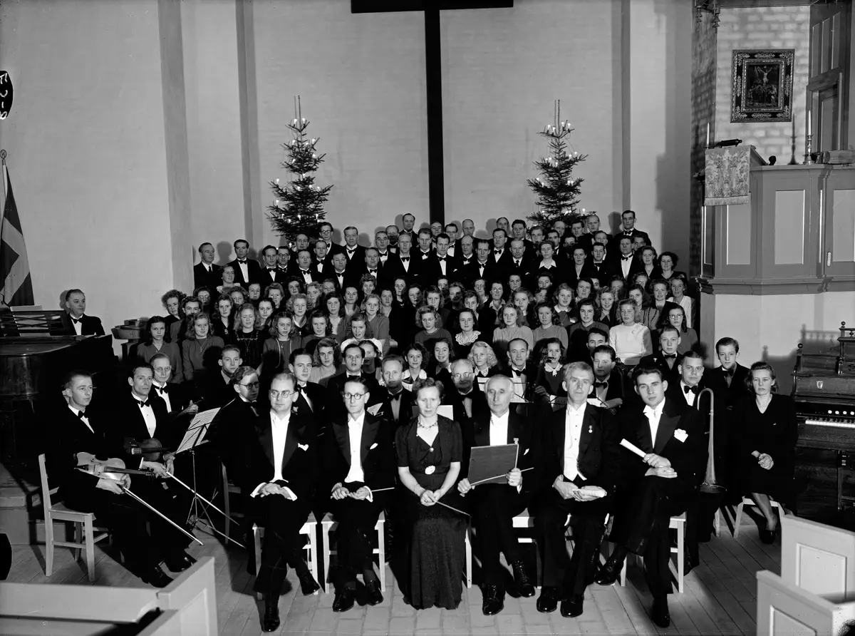 Orkester och körsångare i Nynäshamns kyrka. Konsert som hölls på nyårsafton 1945, med anledning av att Nynäshamn blir stad 1 januari 1946. Längst fram sitter dirigenter, bakom dem sitter en orkester och bakom dem står körsångare. 