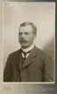 En man i mustasch, klädd i kostym med väst, stärkkrage och slips.
Bröstbild, halvprofil. Ateljéfoto.
Präglat årtal i nhh: 
