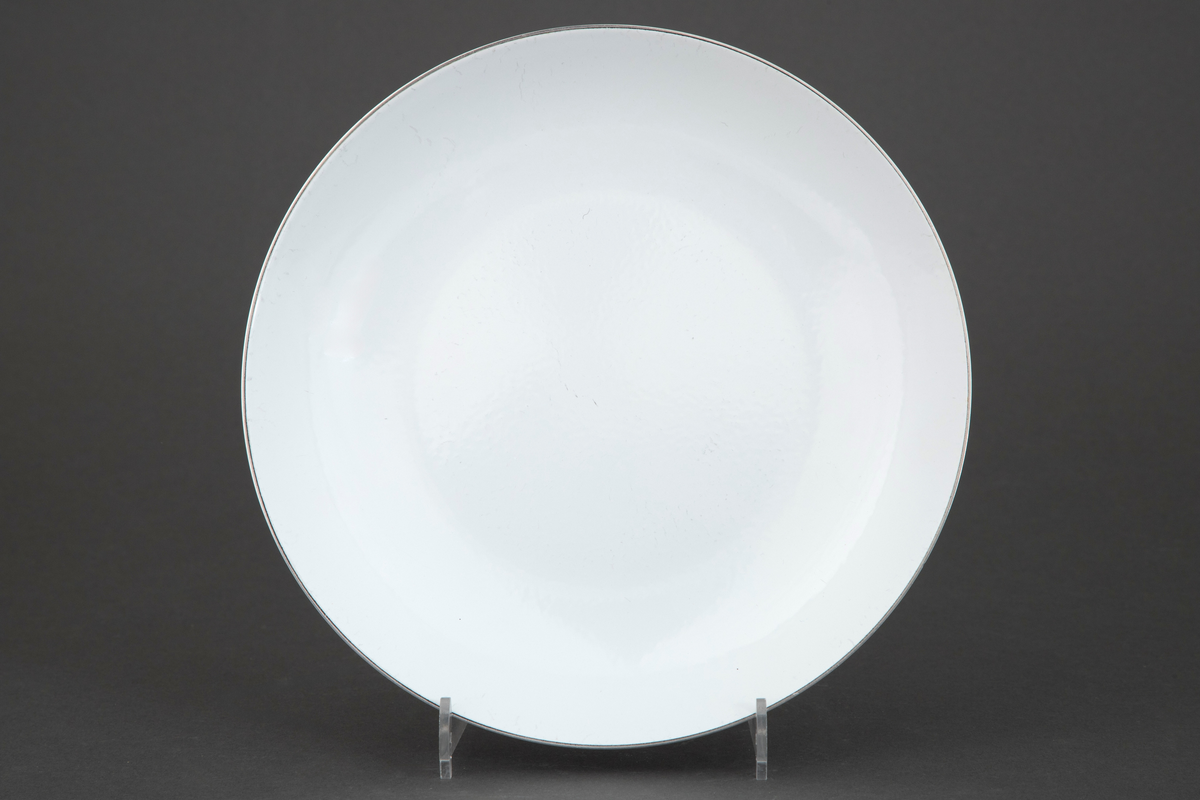 Tallerken i rustfritt stål med pålagt emalje. Rund form med jevnt buede vegger. Oversiden er dekket av hvit opak emalje på umønstret bunn.