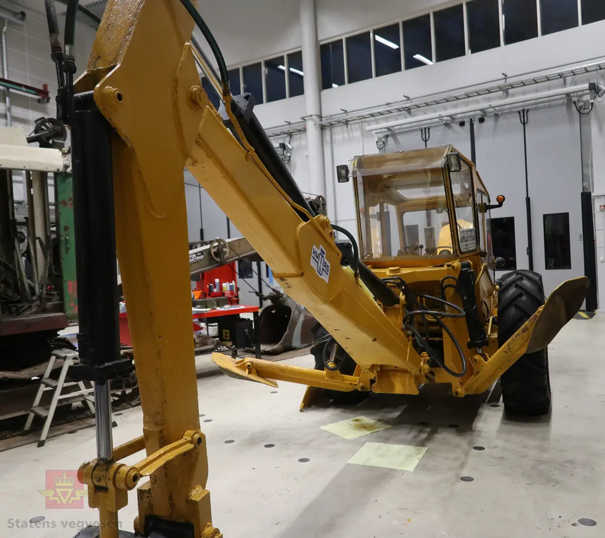 BM-Volvo T-400 traktor med Hymas type 4 graver. Gul, svart og rød traktorgraver lagd i hovedsak av metall, gummi og glass. Merket av produsentene. Dette er en jordbrukstraktor som er påmontert en graver, (gravemaskin), i bakkant. Graveren er hydraulisk drevet og har skuffe og to støtteben. Traktoren er 2-akslet har 6 hjul. To av hjulene er for å kunne bruke traktoren med halvbelter (belter følger med). Motoren er av typen D 913 fra BM, som betyr en tre sylindret firetakts diesel drevet type med slagvolum 2,5 liter. Motoren yter 47 (DIN) Hk. Motoren er bygd med basis fra en Perkins motor. Girkassen har innebygd reduksjons gir som gir åtte gir fremover og to gir bakover. Traktoren har 12 V elektrisk anlegg. Rødt sete merket med BM.
Følgende fulgte med maskinen:
- To skuffer og en hydraulikksentral samt to trekkstenger.
- Fire bilder/tegninger i glass og ramme.
- Regningsblokk.
- Innrammet avisutklipp.