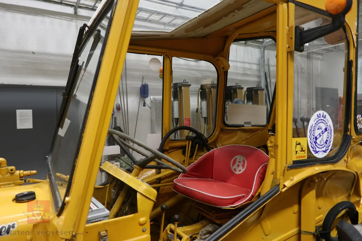 BM-Volvo T-400 traktor med Hymas type 4 graver. Gul, svart og rød traktorgraver lagd i hovedsak av metall, gummi og glass. Merket av produsentene. Dette er en jordbrukstraktor som er påmontert en graver, (gravemaskin), i bakkant. Graveren er hydraulisk drevet og har skuffe og to støtteben. Traktoren er 2-akslet har 6 hjul. To av hjulene er for å kunne bruke traktoren med halvbelter (belter følger med). Motoren er av typen D 913 fra BM, som betyr en tre sylindret firetakts diesel drevet type med slagvolum 2,5 liter. Motoren yter 47 (DIN) Hk. Motoren er bygd med basis fra en Perkins motor. Girkassen har innebygd reduksjons gir som gir åtte gir fremover og to gir bakover. Traktoren har 12 V elektrisk anlegg. Rødt sete merket med BM.
Følgende fulgte med maskinen:
- To skuffer og en hydraulikksentral samt to trekkstenger.
- Fire bilder/tegninger i glass og ramme.
- Regningsblokk.
- Innrammet avisutklipp.