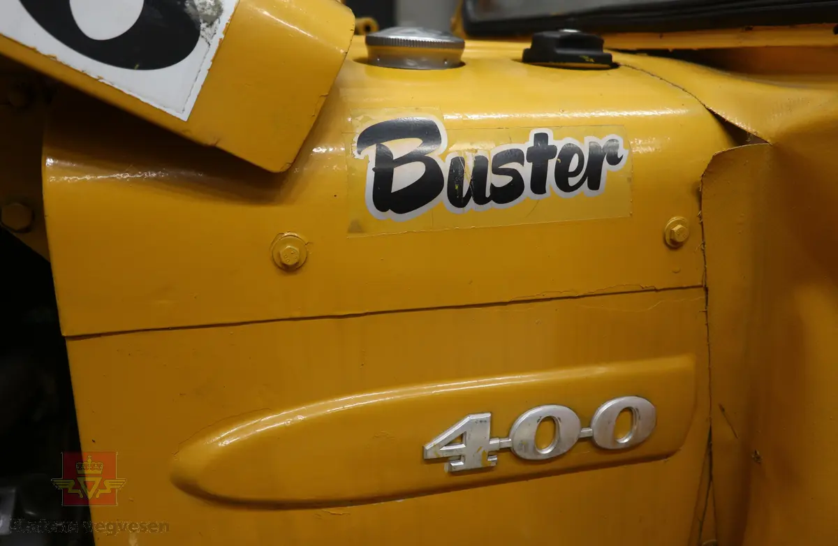 BM-Volvo T-400 traktor med Hymas type 4 graver. Gul, svart og rød traktorgraver lagd i hovedsak av metall, gummi og glass. Merket av produsentene. Dette er en jordbrukstraktor som er påmontert en graver, (gravemaskin), i bakkant. Graveren er hydraulisk drevet og har skuffe og to støtteben. Traktoren er 2-akslet har 6 hjul. To av hjulene er for å kunne bruke traktoren med halvbelter (belter følger med). Motoren er av typen D 913 fra BM, som betyr en tre sylindret firetakts diesel drevet type med slagvolum 2,5 liter. Motoren yter 47 (DIN) Hk. Motoren er bygd med basis fra en Perkins motor. Girkassen har innebygd reduksjons gir som gir åtte gir fremover og to gir bakover. Traktoren har 12 V elektrisk anlegg. Rødt sete merket med BM.
Følgende fulgte med maskinen:
- To skuffer og en hydraulikksentral samt to trekkstenger.
- Fire bilder/tegninger i glass og ramme.
- Regningsblokk.
- Innrammet avisutklipp.