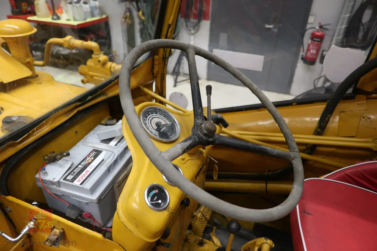 BM-Volvo T-400 traktor med Hymas type 4 graver. Gul, svart og rød traktorgraver lagd i hovedsak av metall, gummi og glass. Merket av produsentene. Dette er en jordbrukstraktor som er påmontert en graver, (gravemaskin), i bakkant. Graveren er hydraulisk drevet og har skuffe og to støtteben. Traktoren er 2-akslet har 6 hjul. To av hjulene er for å kunne bruke traktoren med halvbelter (belter følger med). Motoren er av typen D 913 fra BM, som betyr en tre sylindret firetakts diesel drevet type med slagvolum 2,5 liter. Motoren yter 47 (DIN) Hk. Motoren er bygd med basis fra en Perkins motor. Girkassen har innebygd reduksjons gir som gir åtte gir fremover og to gir bakover. Traktoren har 12 V elektrisk anlegg. Rødt sete merket med BM.
Følgende fulgte med maskinen:
- To skuffer og en hydraulikksentral samt to trekkstenger.
- Fire bilder/tegninger i glass og ramme.
- Regningsblokk.
- Innrammet avisutklipp.