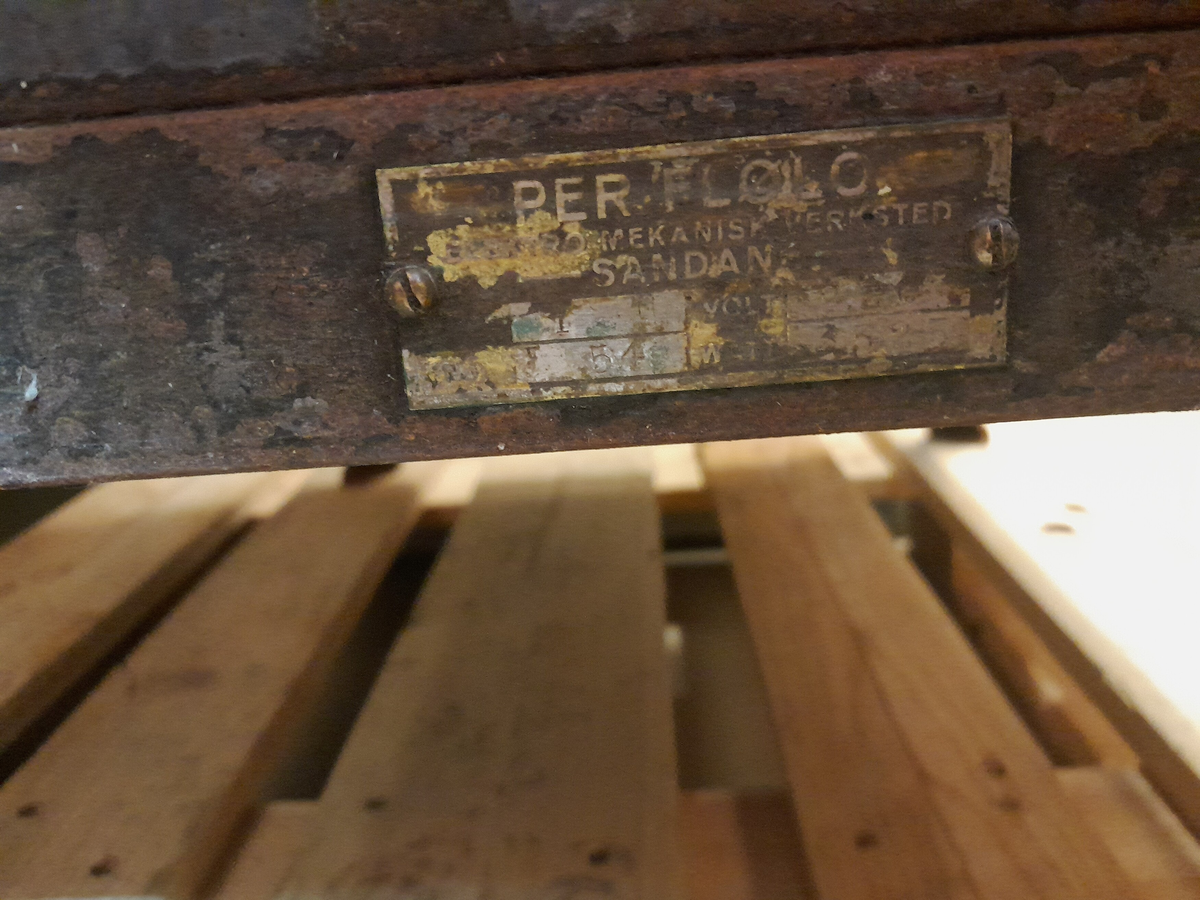 Flølo komfyren. Elektrisk komfyr. Med tank for varmt vatten (oppå bak), og kran for tapping av det varme vatnet framme. To kokeplater oppå. Fem runde brytarar framme i front. Ei uttrekkbar plate under. Omnsdør til å opne inn til steikjeomnen under der att. To plater med handtak inne i steikjeomnen. Komfyren står på fire bein (av jarn).