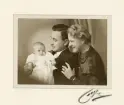 En man och en kvinna med en baby i dopdräkt.
Midjebild. Ateljéfoto.
Oläslig fotografsignatur i nedre högra hörnet.

Carl Rudolf och Margareta Lidén med dottern Elisabeth på dopdagen.