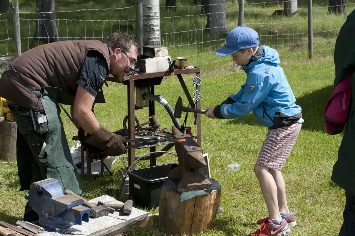 Gutt banker på oppvarmet jern i en utendørs smie. 