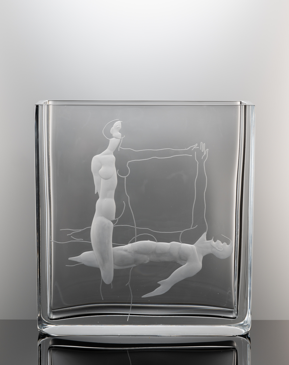 Formgivare: Olle Alberius. Gravör: Anders Svensson. Vas, Expo. Rektangulär, tjockväggig vas med graverat motiv föreställande en kvinna och man utförande en formation.