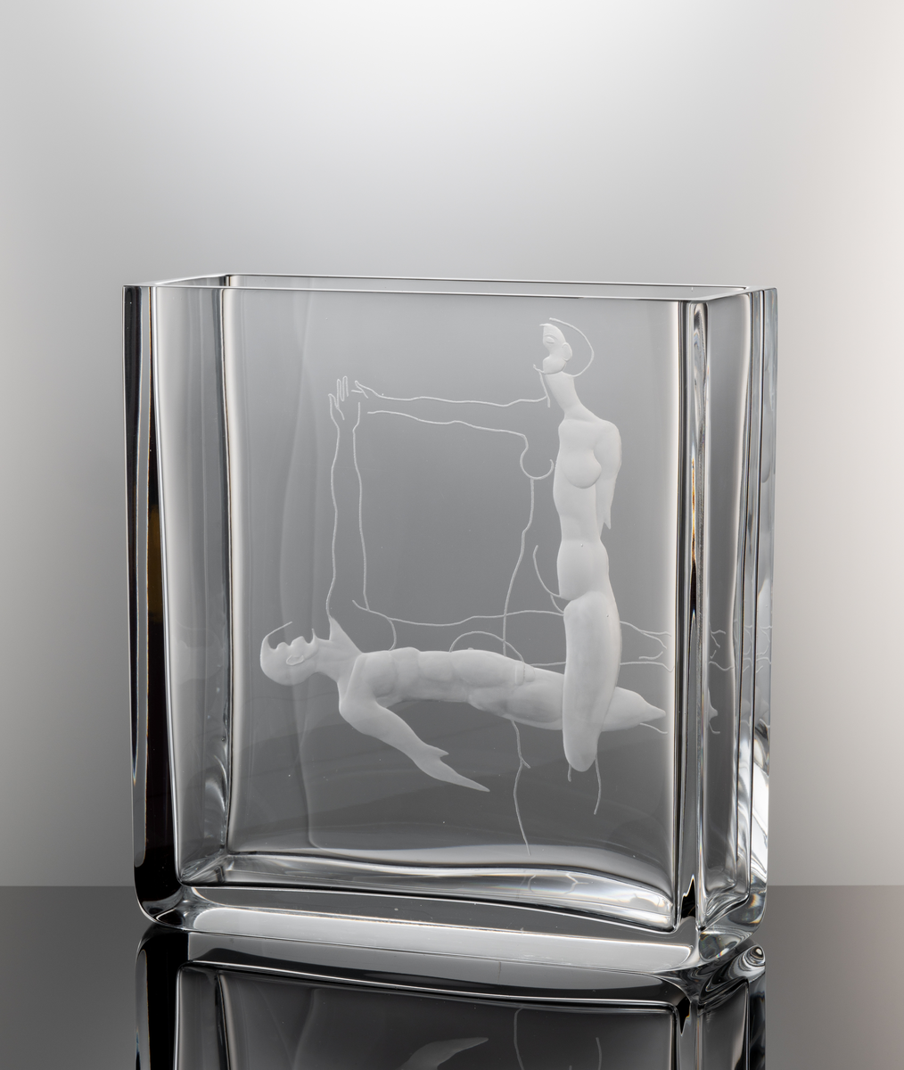 Formgivare: Olle Alberius. Gravör: Anders Svensson. Vas, Expo. Rektangulär, tjockväggig vas med graverat motiv föreställande en kvinna och man utförande en formation.