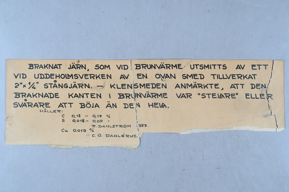 Prov på braknat järn. Tillhörande lapp med notering: "Braknat järn, som vid brunvärme utsmitts av ett vid Uddeholmsverken av en ovan smed tillverkat 2'x 1¤' stångjärn. -Klensmeden anmärkte, att den braknade kanten i brunvärme var 'stelare' eller svårare att böja än den hela. Håller: C 0,18-0,19 %, S 0,0018-0,02 %, R. Dahlström. Cu 0,012 %. C. G. Dahlérus. 1883."
