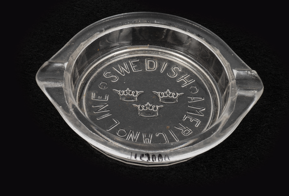 Askkoppar i pressglas. Runda med fasettmönstrade sidor, tunn kant upptill med två "cigaretthållare". Gjutet mönster på undersidan av den genomskinliga botten: "SWEDISH AMERICAN LINE" i cirkel kring SAL:s emblem med tre kronor.