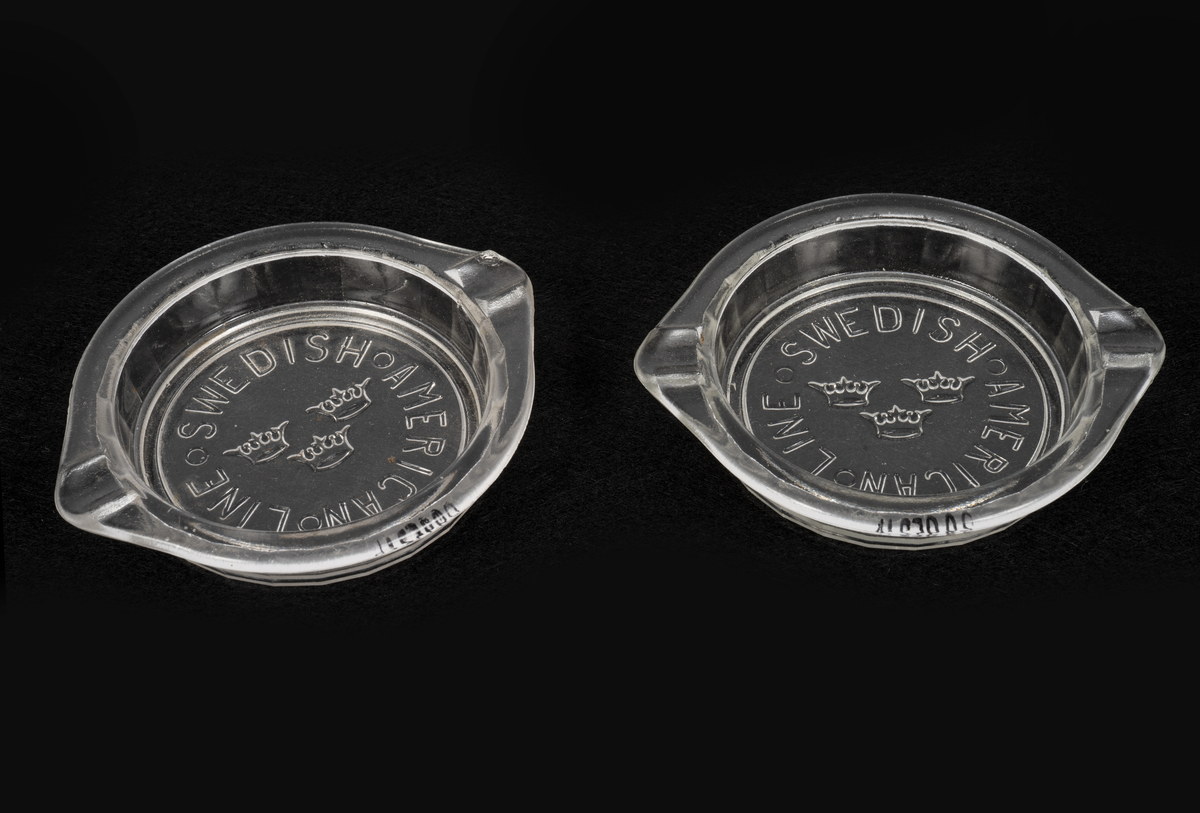 Askkoppar i pressglas. Runda med fasettmönstrade sidor, tunn kant upptill med två "cigaretthållare". Gjutet mönster på undersidan av den genomskinliga botten: "SWEDISH AMERICAN LINE" i cirkel kring SAL:s emblem med tre kronor.