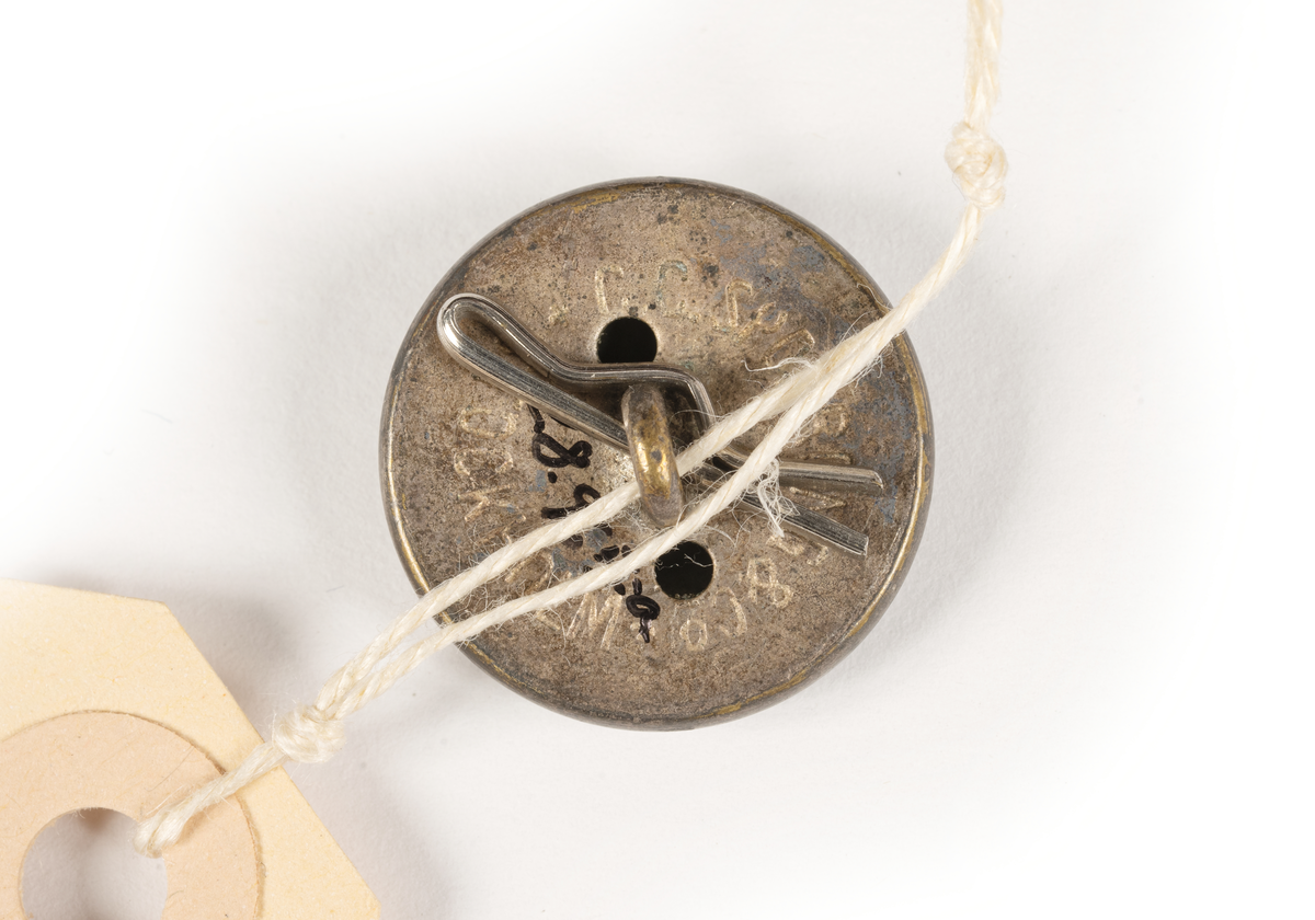 Runda, konvexa, metallknappar med präglat ankare omgivet av SAL:s emblem med tre kronor mot räfflad bakgrund, inramat av en slät bård i form av ett band med texten SVENSKA AMERIKA LINIEN, avslutas mot kanten av en repdekor.

Baksidan pålödd ögla för fästande av knappen på plagg, två hål, texten: C.C. SPORRONG & CO STOCKHOLM.