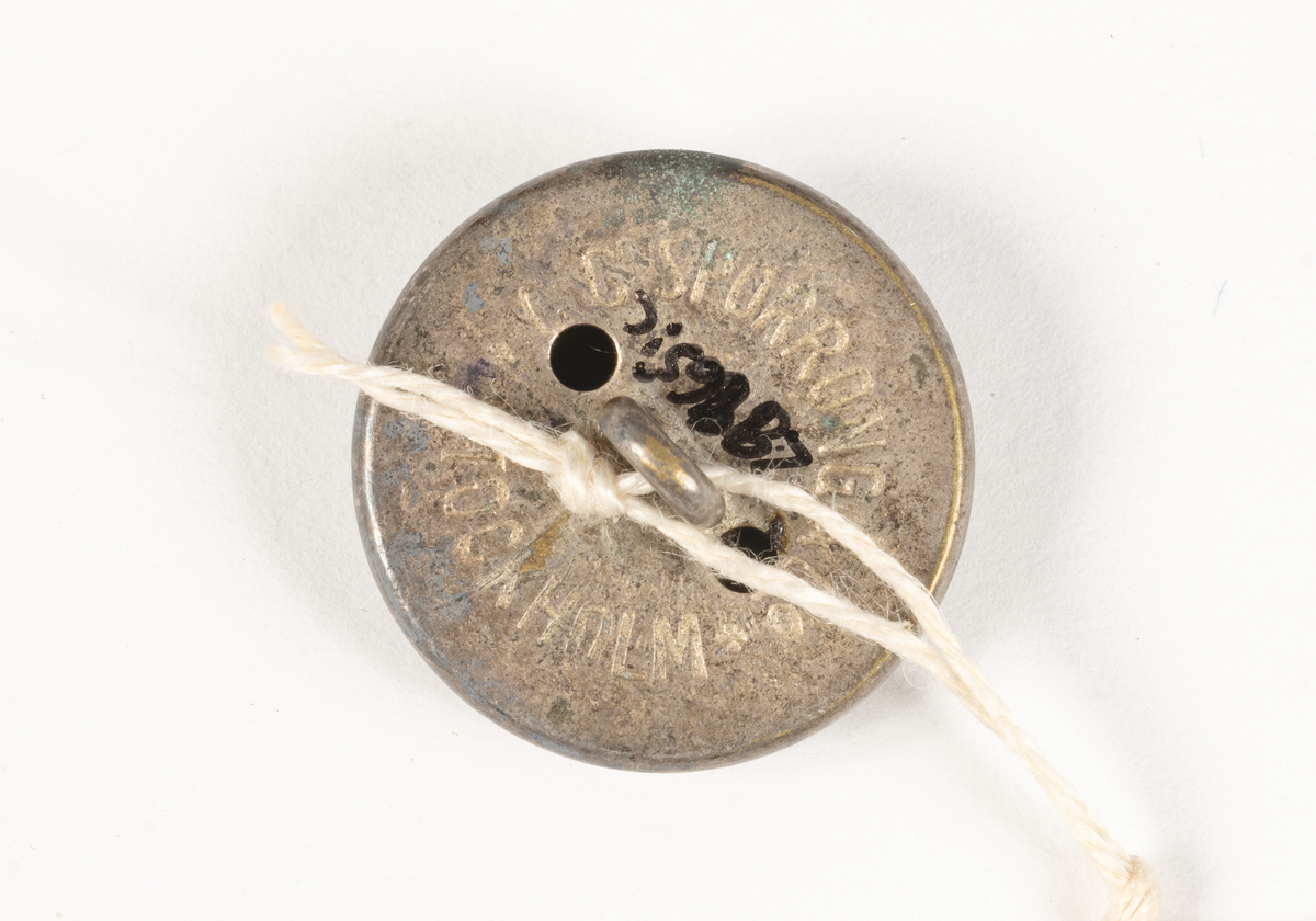 Runda, konvexa, metallknappar med präglat ankare omgivet av SAL:s emblem med tre kronor mot räfflad bakgrund, inramat av en slät bård i form av ett band med texten SVENSKA AMERIKA LINIEN, avslutas mot kanten av en repdekor.

Baksidan pålödd ögla för fästande av knappen på plagg, två hål, texten: C.C. SPORRONG & CO STOCKHOLM.