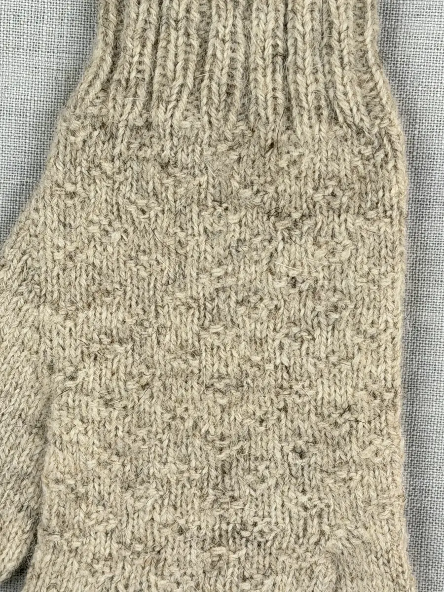 En stickad fingervante, med mudd i 2-2 resår (2 räta och 2 aviga maskor) och vante mönstrad med aviga maskor på slätstickning, av 2-trådigt ullgarn.