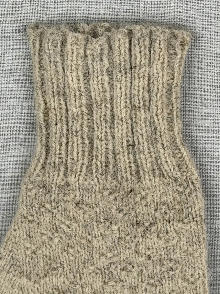 En stickad fingervante, med mudd i 2-2 resår (2 räta och 2 aviga maskor) och vante mönstrad med aviga maskor på slätstickning, av 2-trådigt ullgarn.