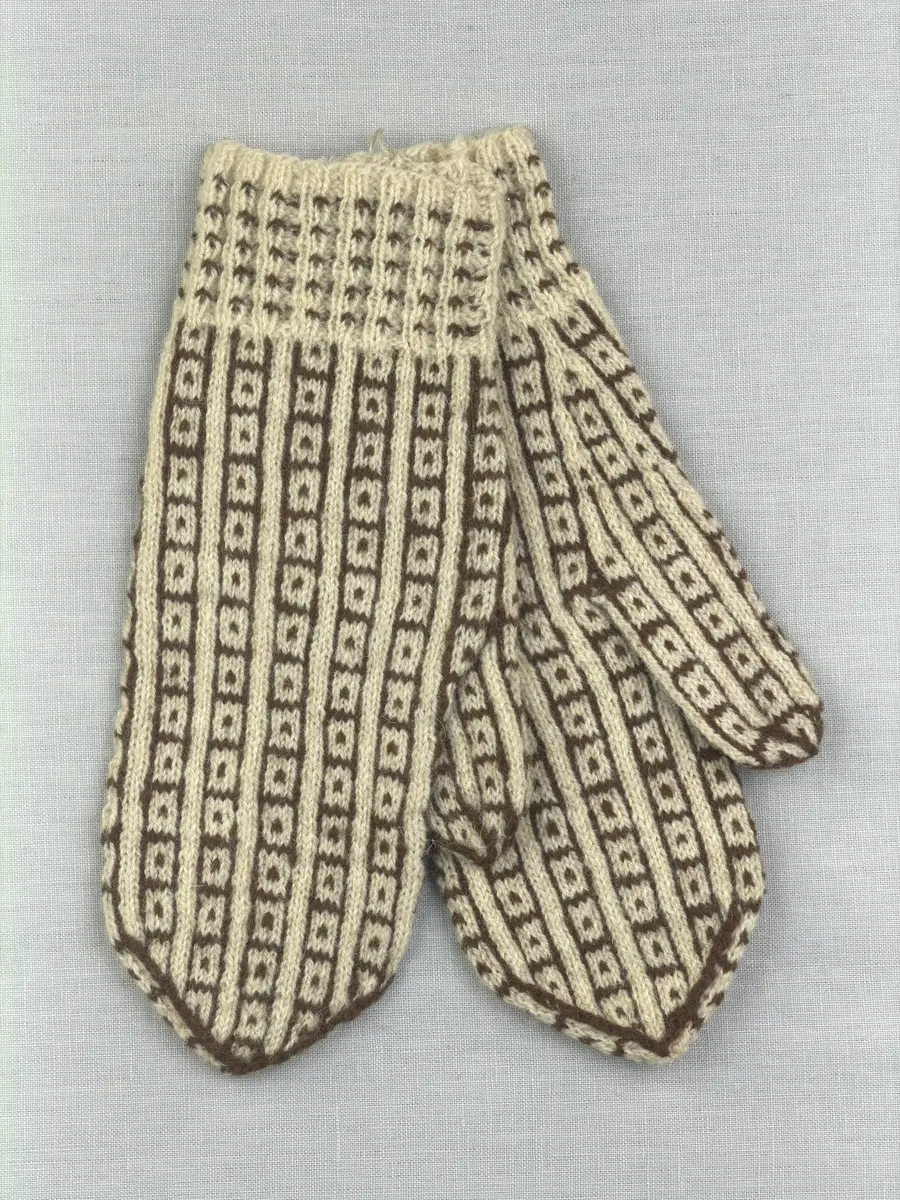 En stickad fingervante, med mönstrad mudd i 2-2 resår (2 räta och 2 aviga maskor) och mönsterstickad vante i slätstickning, av 2-trådigt ullgarn.