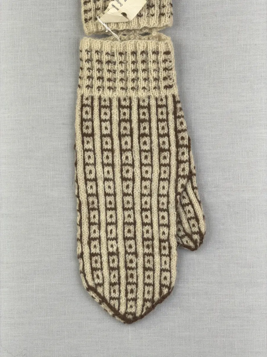 En stickad fingervante, med mönstrad mudd i 2-2 resår (2 räta och 2 aviga maskor) och mönsterstickad vante i slätstickning, av 2-trådigt ullgarn.