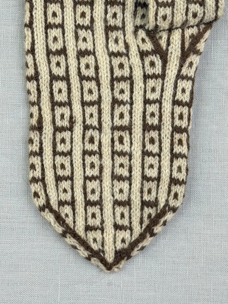 En stickad fingervante, med mönstrad mudd i 2-2 resår (2 räta och 2 aviga maskor) och mönsterstickad vante i slätstickning, av 2-trådigt ullgarn.