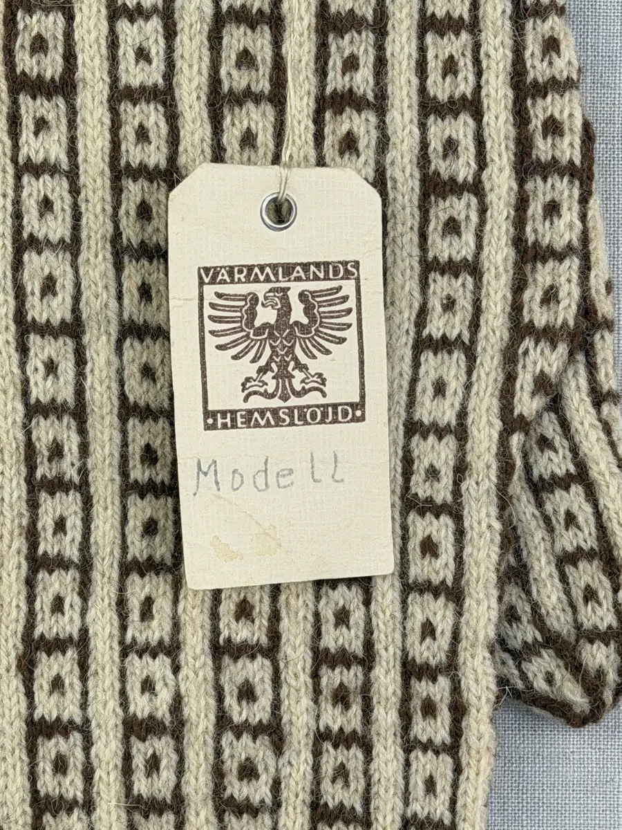 En stickad fingervante, med mönstrad mudd i 2-2 resår (2 räta och 2 aviga maskor) och mönsterstickad vante i slätstickning, av 2-trådigt ullgarn.