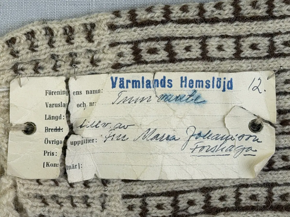 En stickad fingervante, med mönstrad mudd i 2-2 resår (2 räta och 2 aviga maskor) och mönsterstickad vante i slätstickning, av 2-trådigt ullgarn.