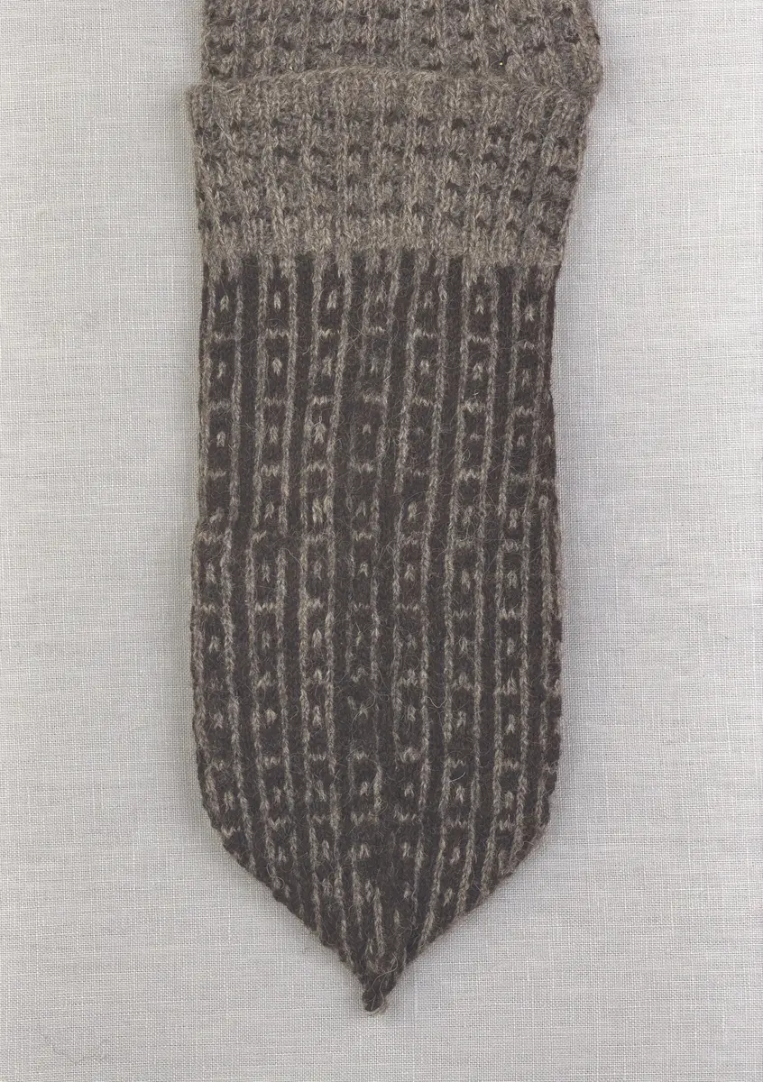 En stickad fingervante, med mönstrad mudd i 2-2 resår (2 räta och 2 aviga maskor) och mönsterstickad vante i slätstickning, av 2-trådigt ullgarn.