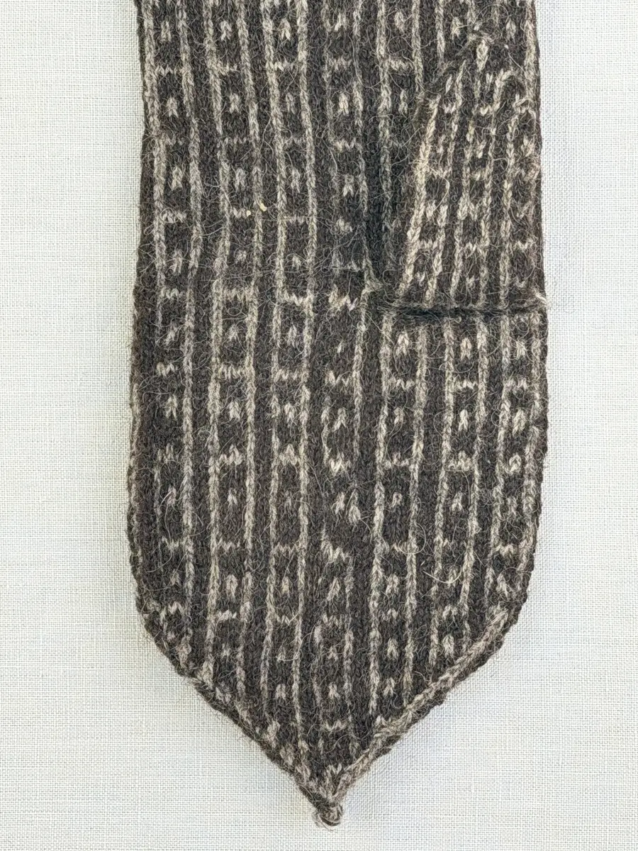En stickad fingervante, med mönstrad mudd i 2-2 resår (2 räta och 2 aviga maskor) och mönsterstickad vante i slätstickning, av 2-trådigt ullgarn.