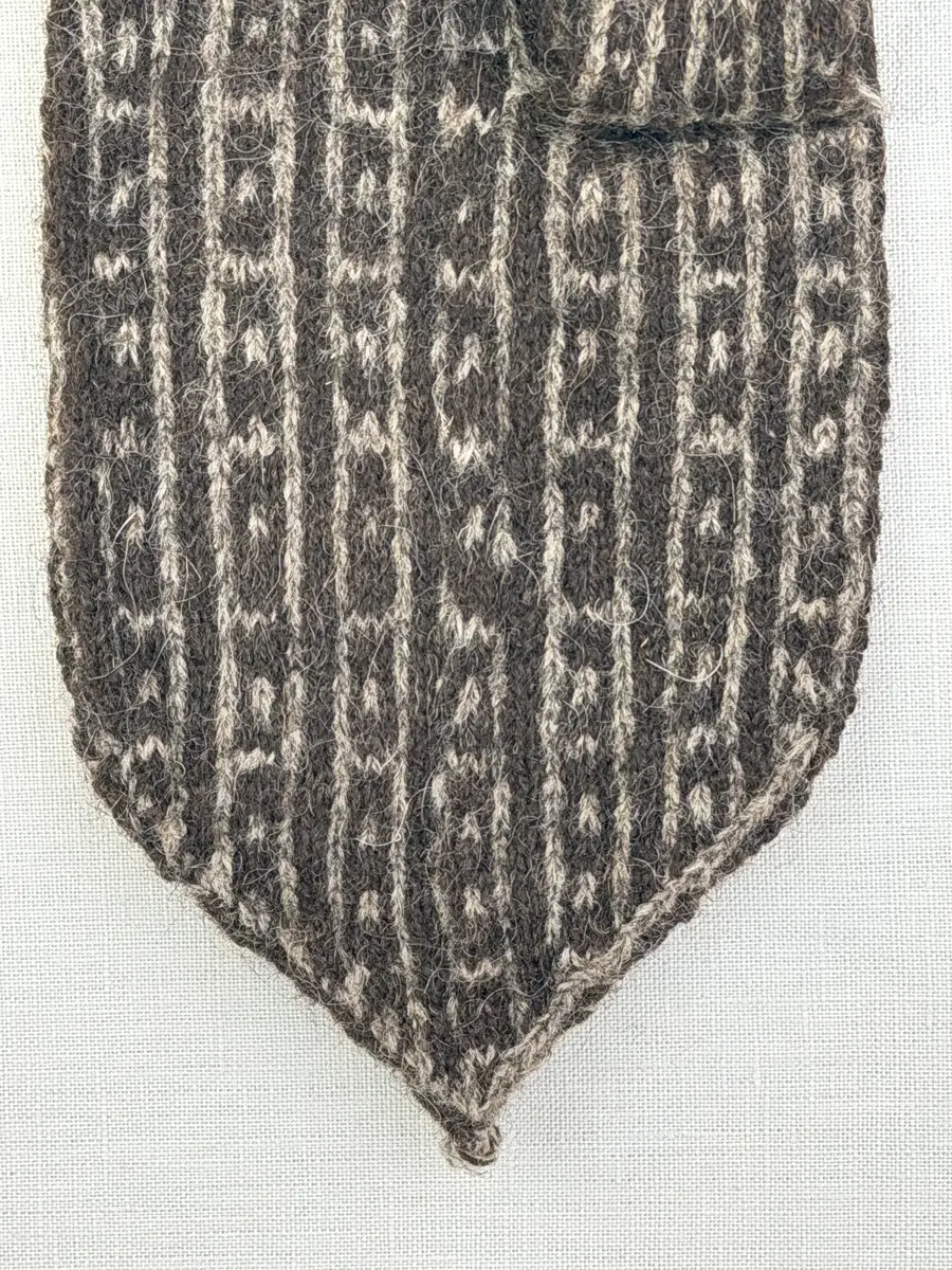 En stickad fingervante, med mönstrad mudd i 2-2 resår (2 räta och 2 aviga maskor) och mönsterstickad vante i slätstickning, av 2-trådigt ullgarn.