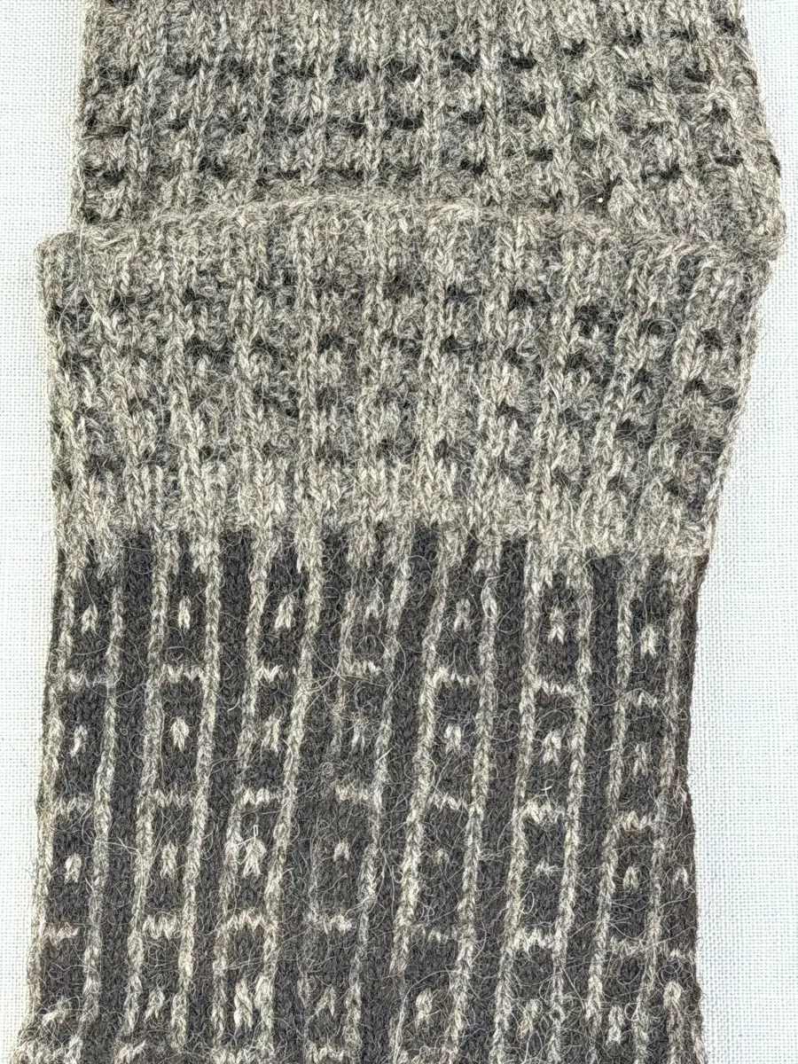 En stickad fingervante, med mönstrad mudd i 2-2 resår (2 räta och 2 aviga maskor) och mönsterstickad vante i slätstickning, av 2-trådigt ullgarn.