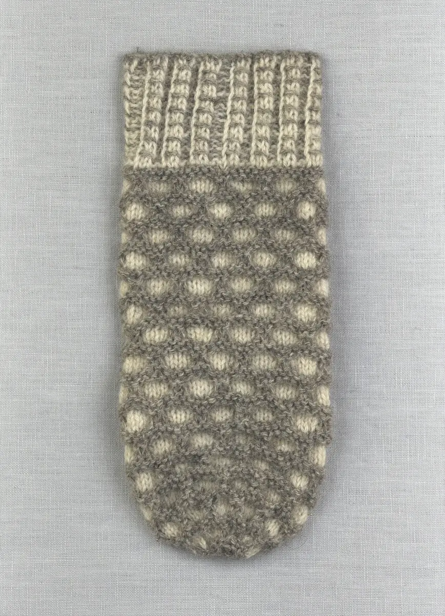 En stickad tumvante, med mönstrad mudd i 2-2 resår (2 räta och 2 aviga maskor) och vante i hålkrus-stickning, av 3-trådigt ullgarn.