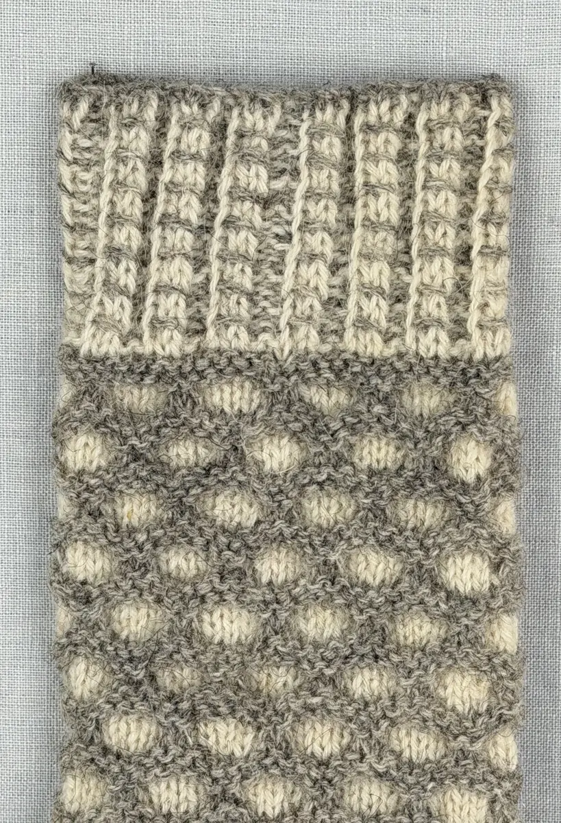 En stickad tumvante, med mönstrad mudd i 2-2 resår (2 räta och 2 aviga maskor) och vante i hålkrus-stickning, av 3-trådigt ullgarn.