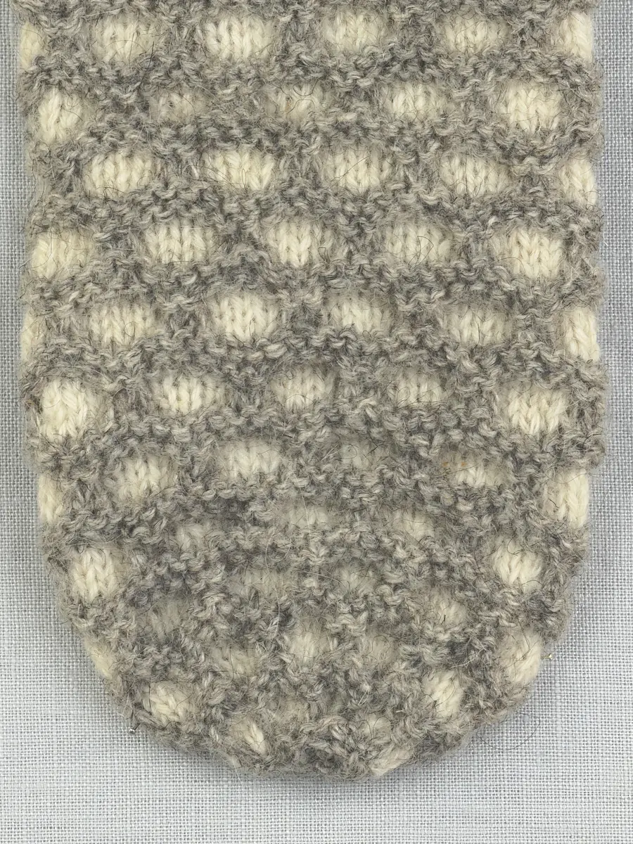 En stickad tumvante, med mönstrad mudd i 2-2 resår (2 räta och 2 aviga maskor) och vante i hålkrus-stickning, av 3-trådigt ullgarn.