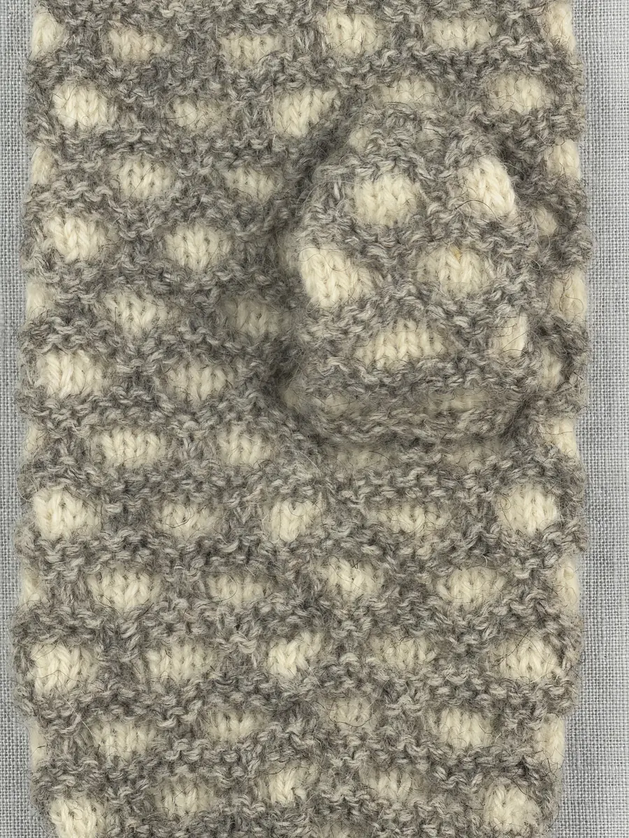 En stickad tumvante, med mönstrad mudd i 2-2 resår (2 räta och 2 aviga maskor) och vante i hålkrus-stickning, av 3-trådigt ullgarn.