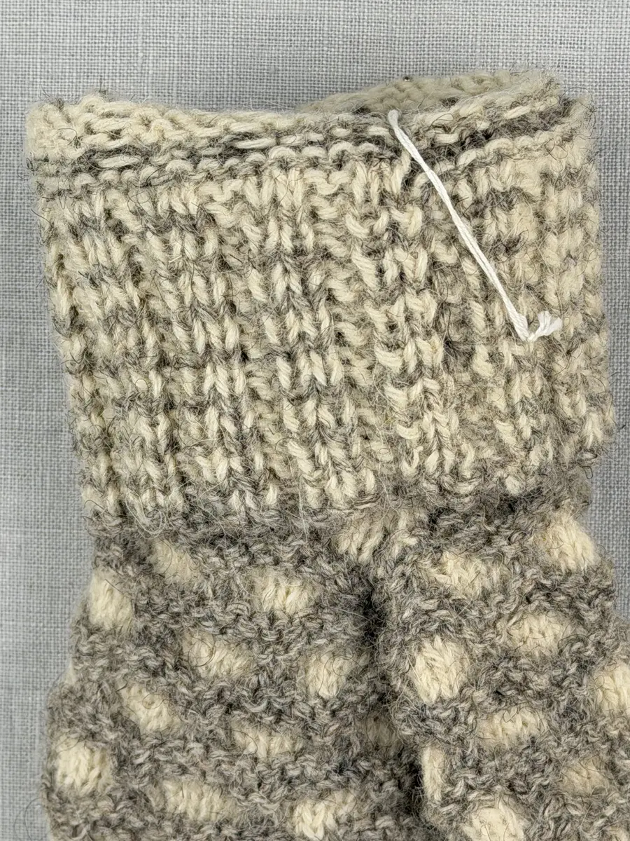 En stickad tumvante, med mönstrad mudd i 2-2 resår (2 räta och 2 aviga maskor) och vante i hålkrus-stickning, av 3-trådigt ullgarn.