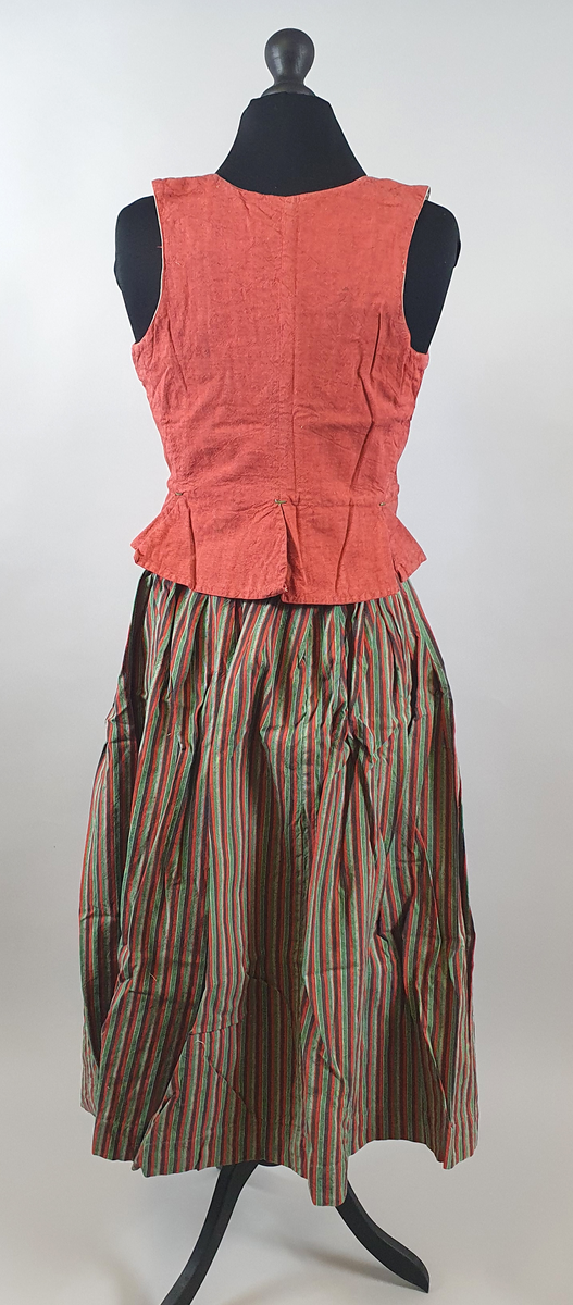 Rødt liv av lin, med seks skjøter (flak) somskår ut fra livlinjen. Metallhemper i åpningen foran. Livet er fôret med ubleket bomull. Brodert navn på innsiden av forstykket.