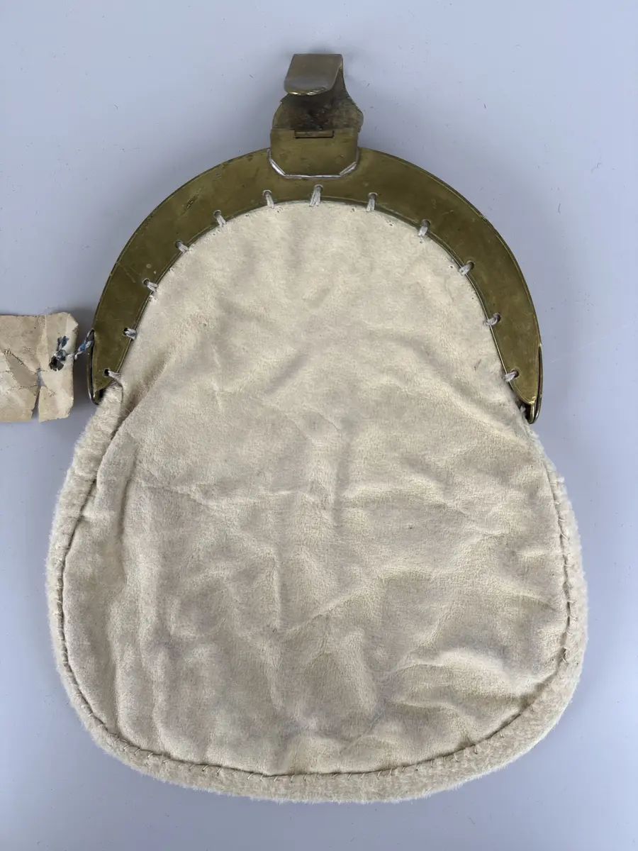 Kjolsäck till dräkt för kvinna från Delsbo socken, Hälsingland. Modell med bygel. Framstycke av svart ylletyg, kläde, med applikationer av rött och grönt ylletyg, fastsydda med tenntrådsbroderi. Motiv: i mitten en grön utklippt figur, omgiven upptill och nertill av röda figurer, alla med konturerna förstärkta med broderi. Foder av tryckt fabrikstillverkat bomullstyg, "persiskt" mönster i många färger. Kantad med remsa av vitt rakat fårskinn. Bakstycke av sämskskinn. Bygel med snäpplås och hake, båda med graverad dekor. Märkt på haken med gravyr: B.E.D.