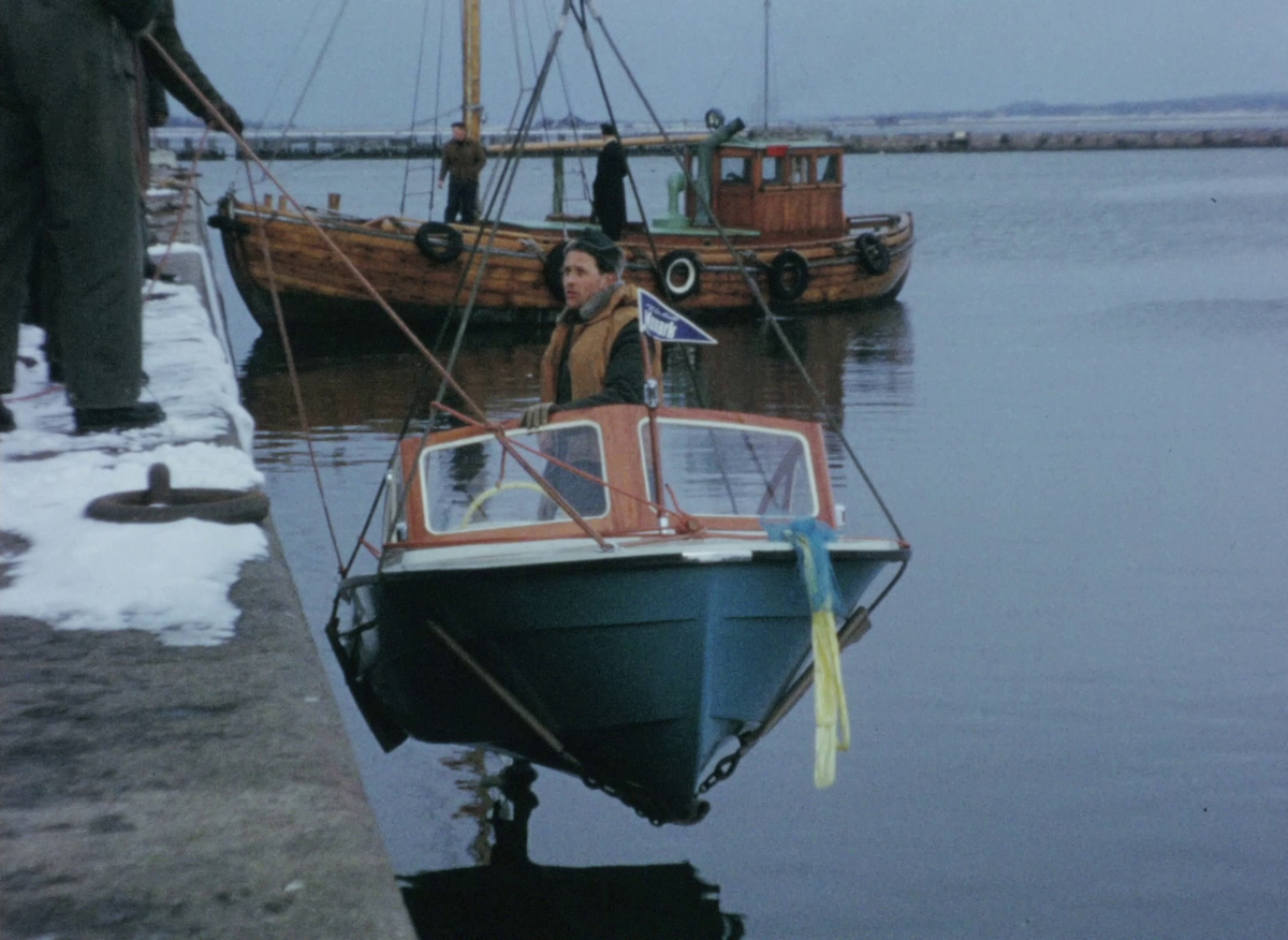 Färgfilm ur Monark-Crescents arkiv som visar båtdop samt testkörning med företagets olika glasfiberbåtsmodeller vid Varbergs kust.


En man drar ut en båtvagn lastad med en mindre motorbåt på en asfalterad plan. En en något större campingbåt med kabin dras iväg på släp med bil. I nästa klipp hänger campingbåten i vajrar över en snöig plan utomhus, omgiven av män klädda i overaller, kappor, mössor och hattar. De genomför en dopceremoni där en glasflaska krossas mot fören så att innehållet skummar ut över båten. Båtkranen sänker sedan ned båten i vattnet intill kajen, varefter två män testkör båten. Under färden passerar man bland annat Stora Skrivareklippan.


En eka i glasfiber som bär texten "Monark test 21" sjösätts med möda i den stormiga Badhusviken. Varbergs kallbahus ses stå på pålar ute i vattnet. Tre män i heltäckande regnkläder hjälps åt att få ut båten från en stenig strandkant utanför Norra fästningshörnan, varav en sitter vid årorna. Ute på vattnet försöker mannen vid årorna ro mot de höga vågorna. Deras svall lyfter båten uppåt och flera gånger slår de över bogen ner i skrovet.


Fler motorbåtar testkörs: en annan modell med kabinrutor och texten "Monark test 19" på sidan, samt en motordriven eka med texten "Monark test 20". Även "Monark test 21" testkörs med motor.